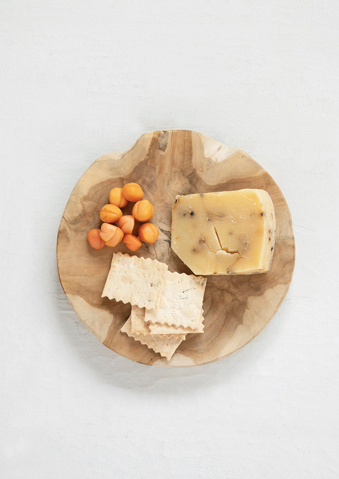 A round teak board with cheese and crackers.