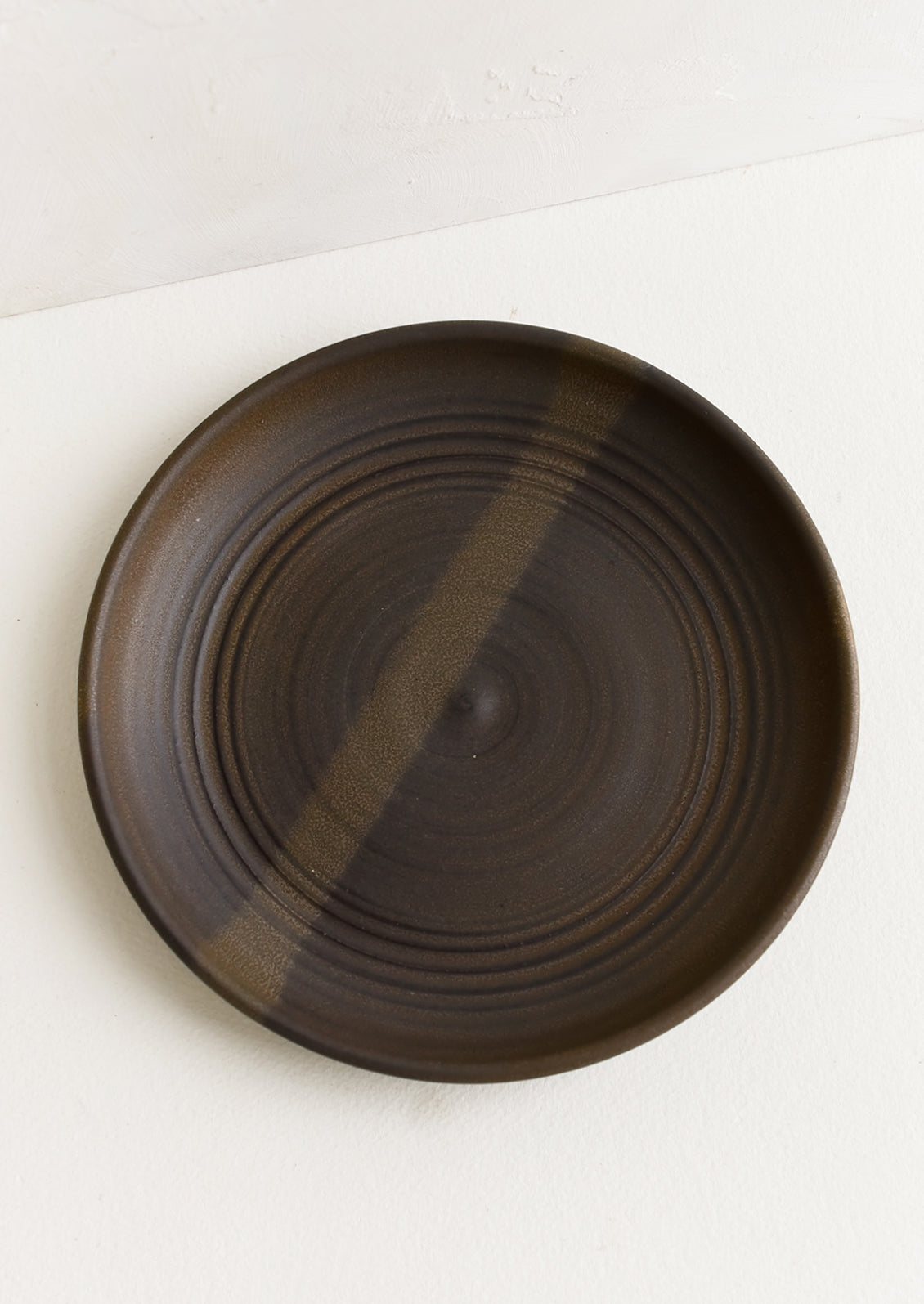 A ceramic side plate in a matte dark brown glaze.
