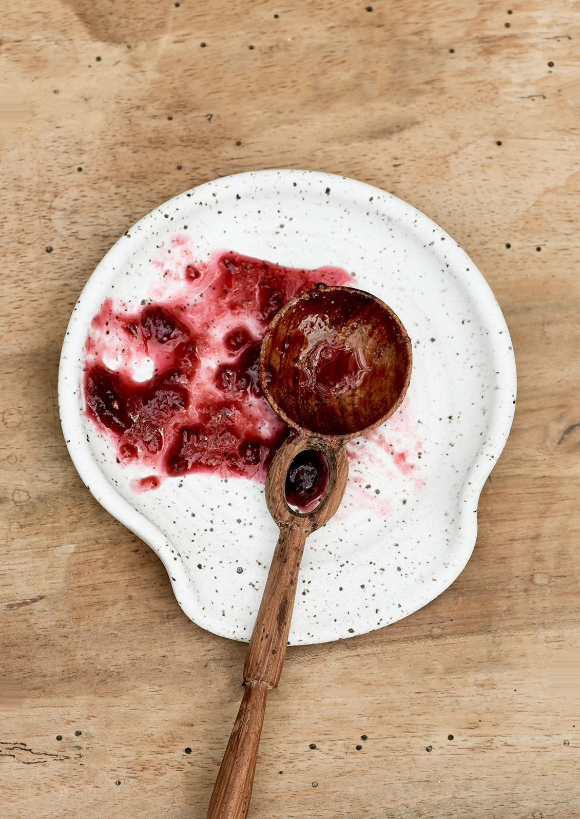A wooden spoon with raspberry jam on ceramic spoon rest.