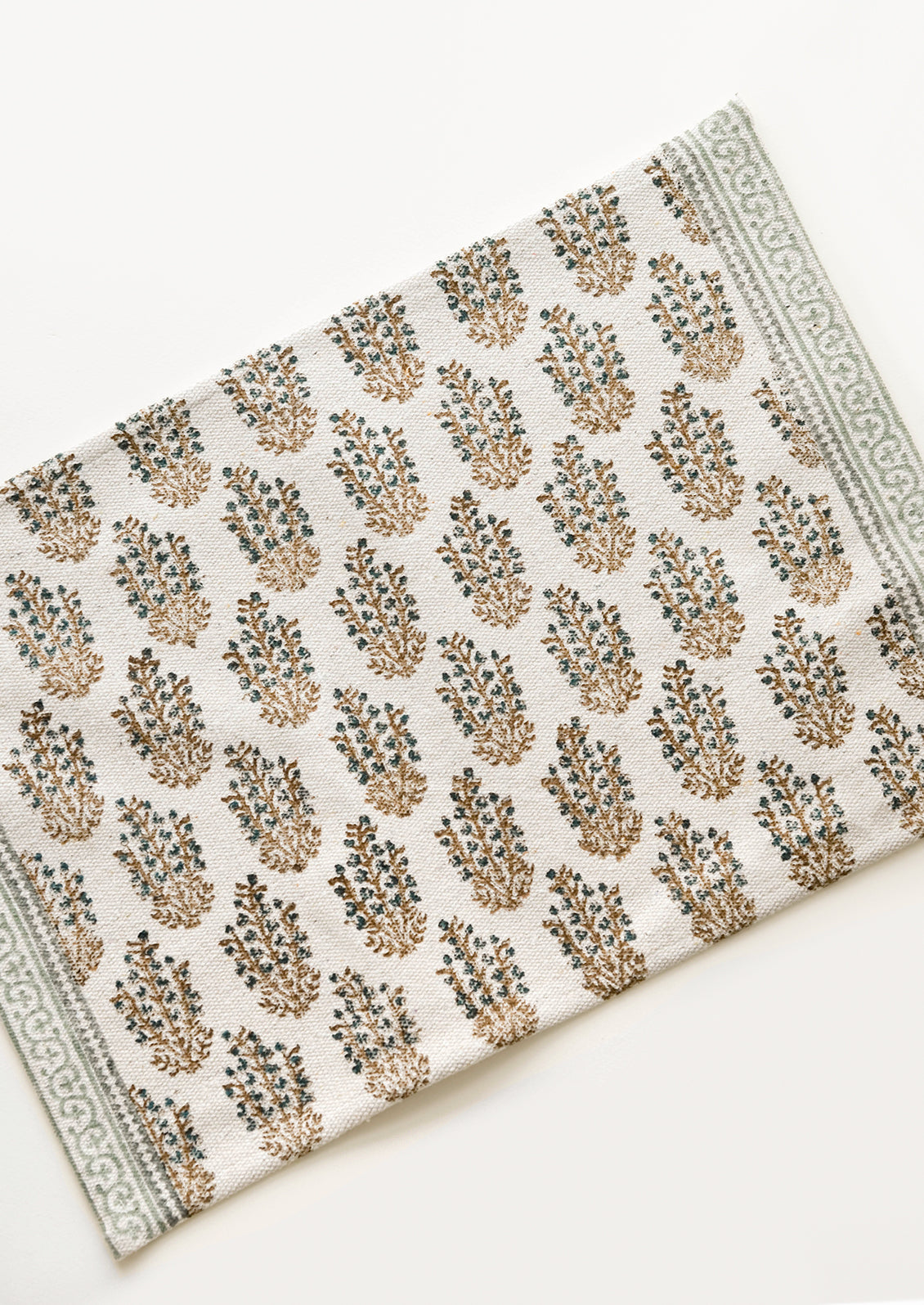 An ivory rectangular cotton placemat with green floral pattern.