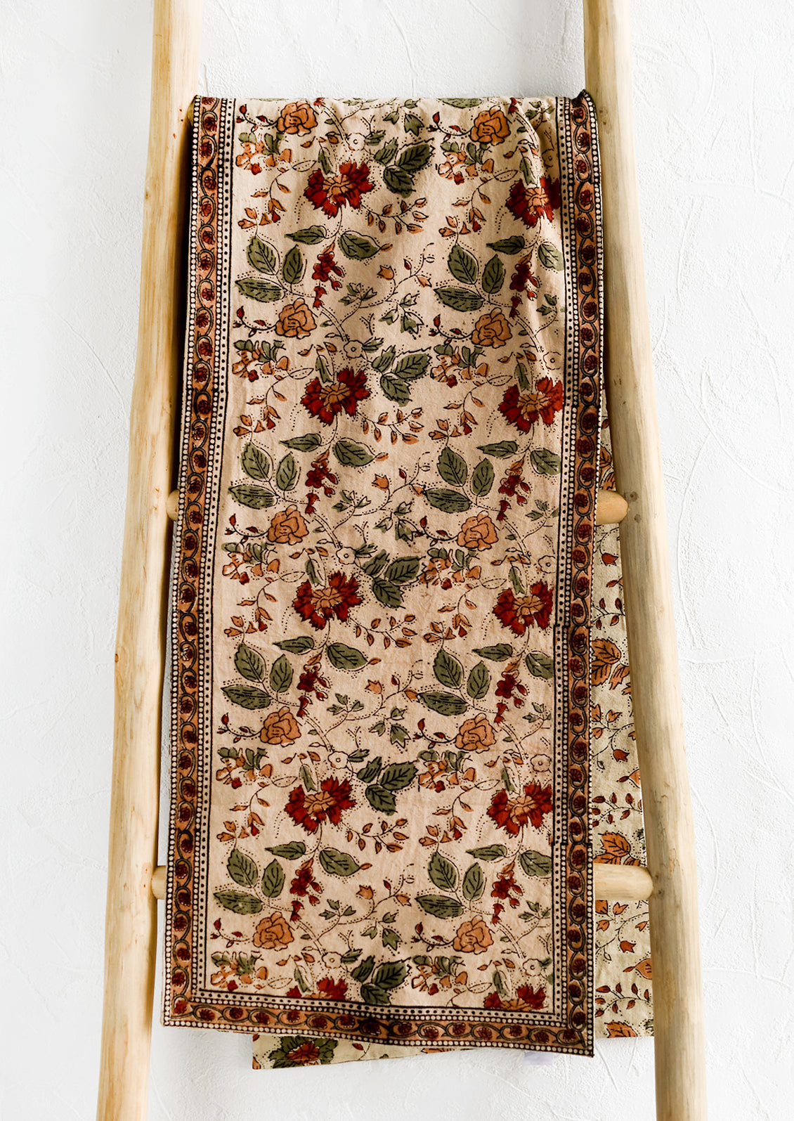 A block printed table runner in crimson, green and beige floral print.