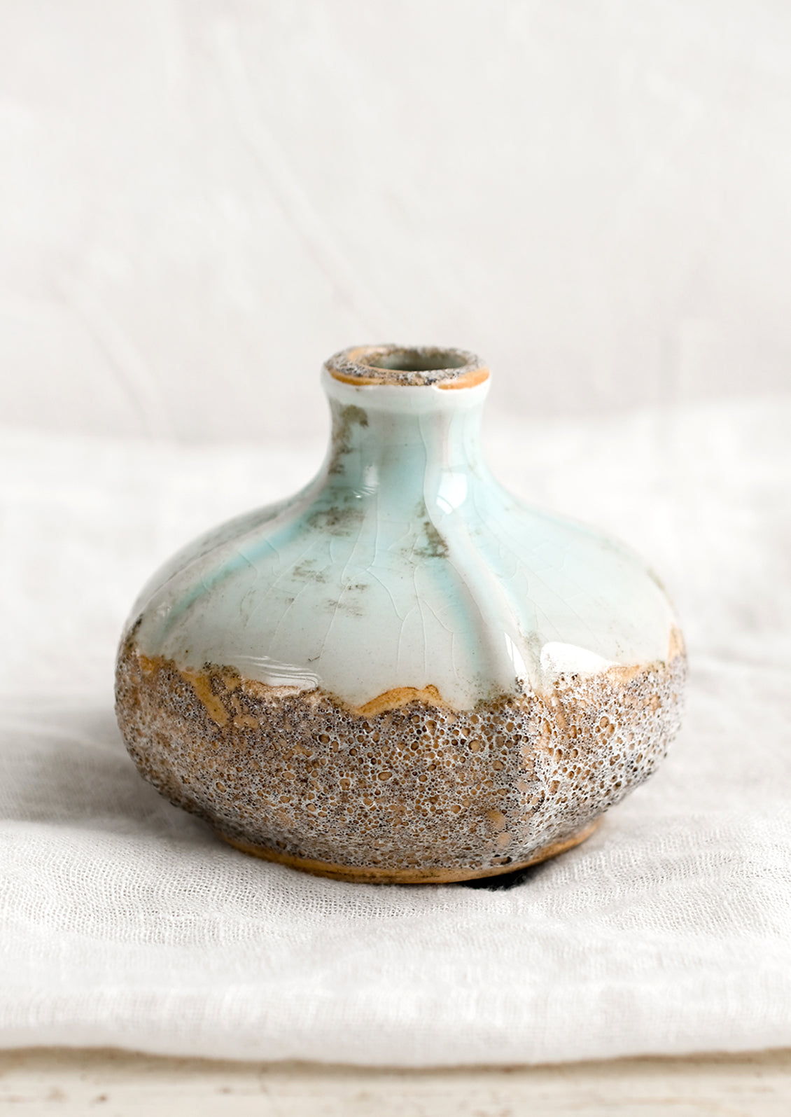 A short bud vase in distressed seafoam and brown sandy glaze.