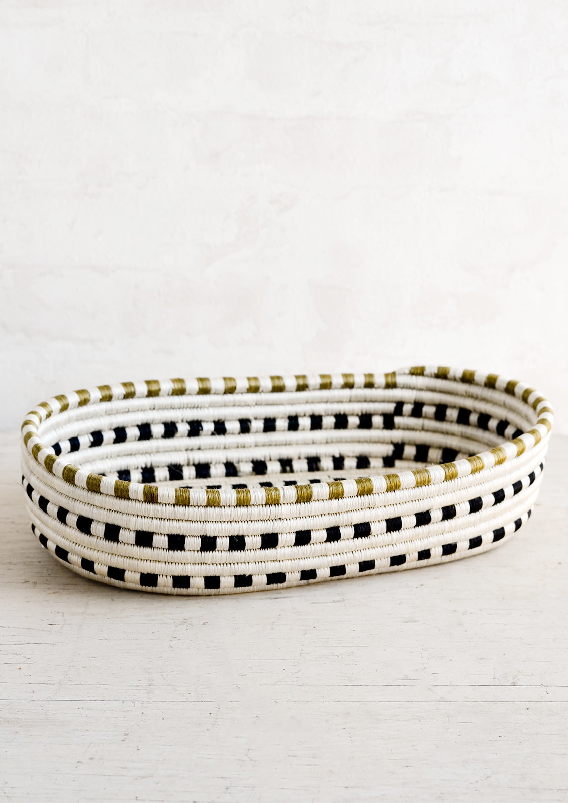 An oval shaped basket made from woven sweetgrass in black and white dash pattern.