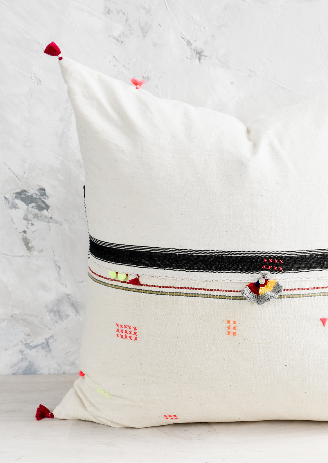 A square throw pillow with neon embroidery and tassel detailing.