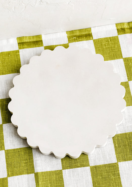 A concrete trivet with scalloped edges in cream.
