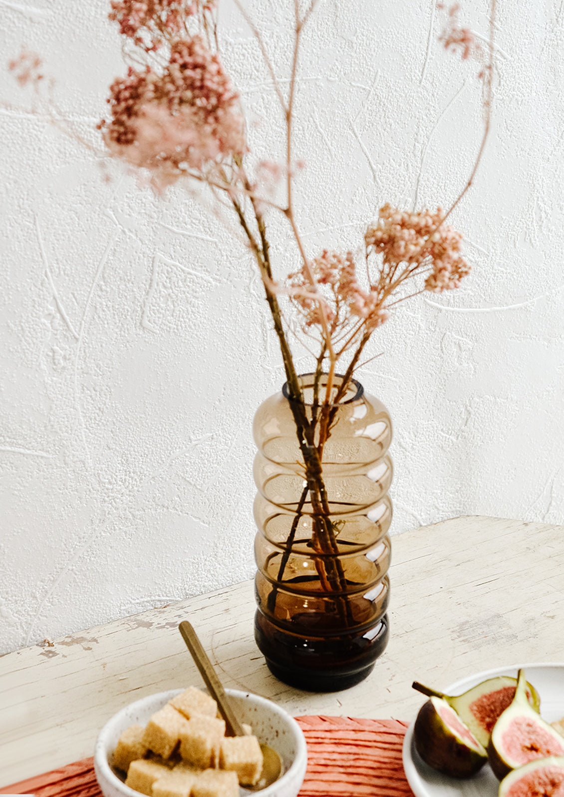 A clear brown glass vase in a curvy silhouette with dried pink flowers.
