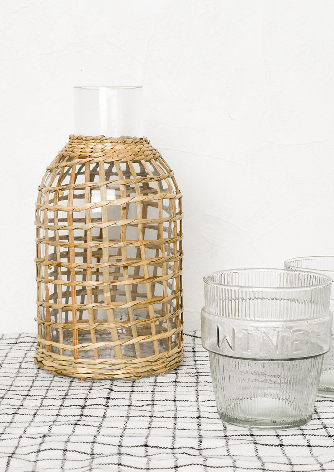 A seagrass wrapped carafe with two glasses.