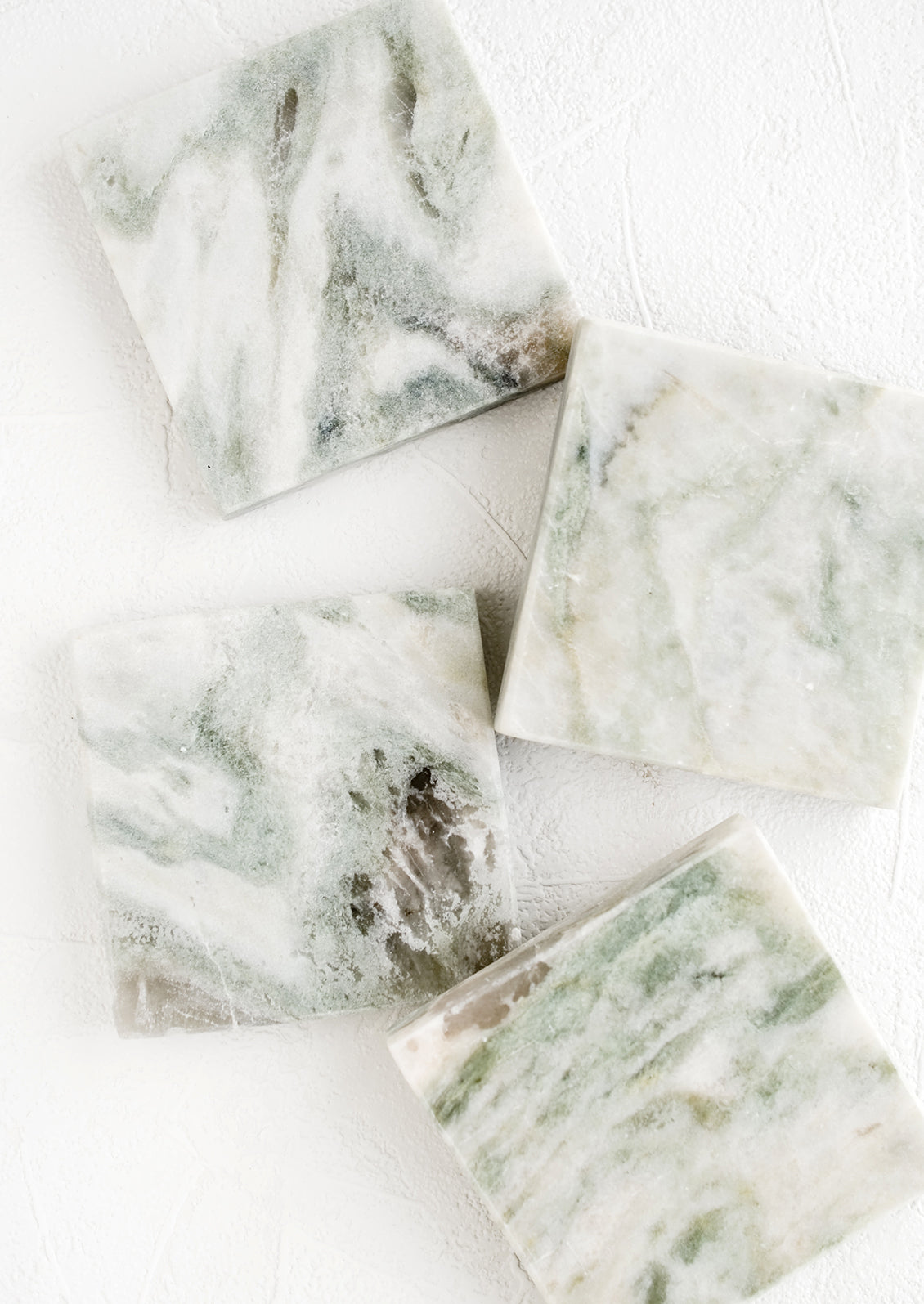 Four square marble coasters with variegated tones of green, white and grey.