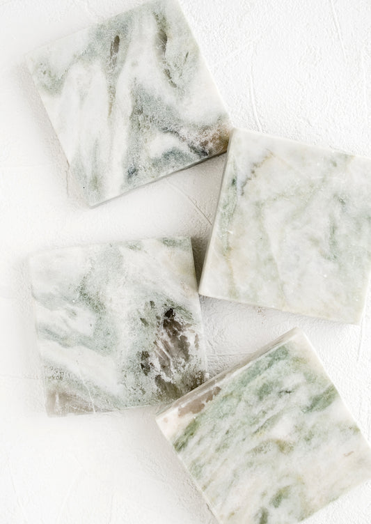 Four square marble coasters with variegated tones of green, white and grey.