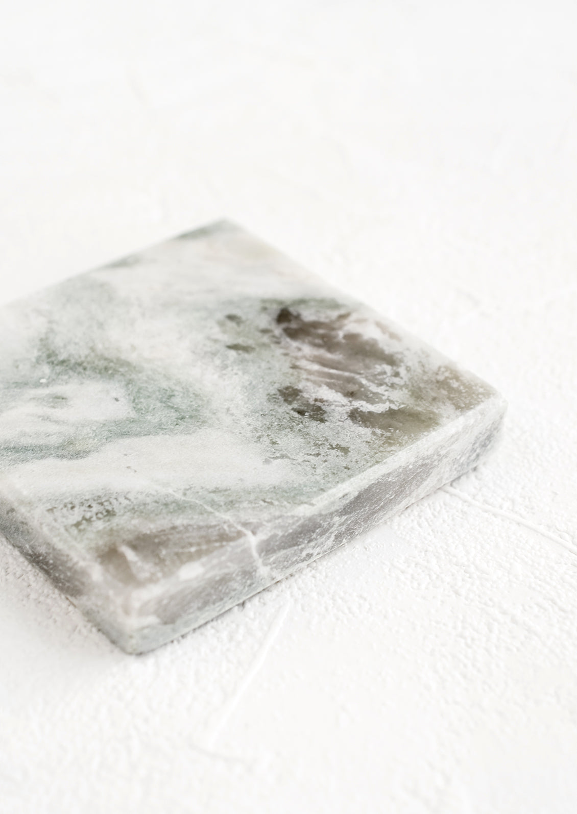 A thick marble coaster in variegated tones of green, grey and white.