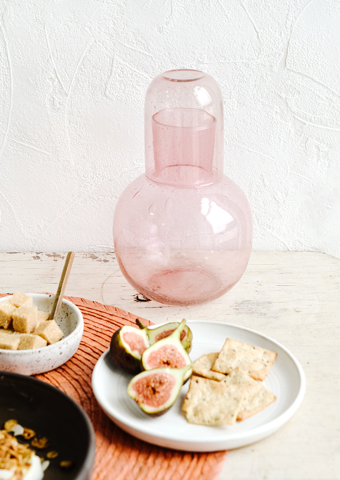 A tabletop set with plates holding figs, crackers and sugar cubes.