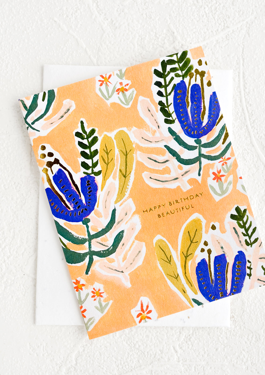 A peach colored greeting card with whimsical floral print and small gold text reading "Happy Birthday Beautiful"