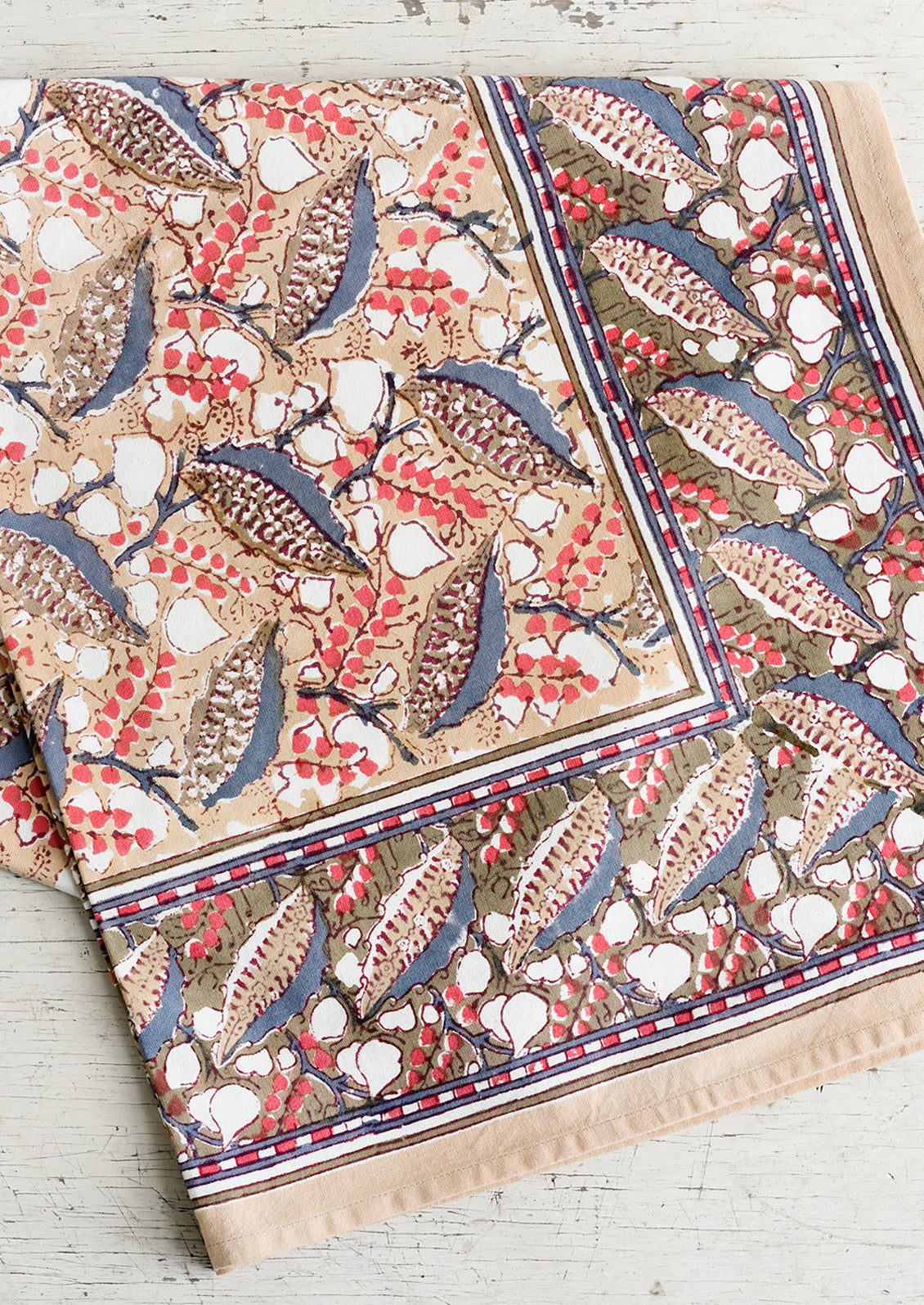 A block print tablecloth with tan, red and slate blue floral print.