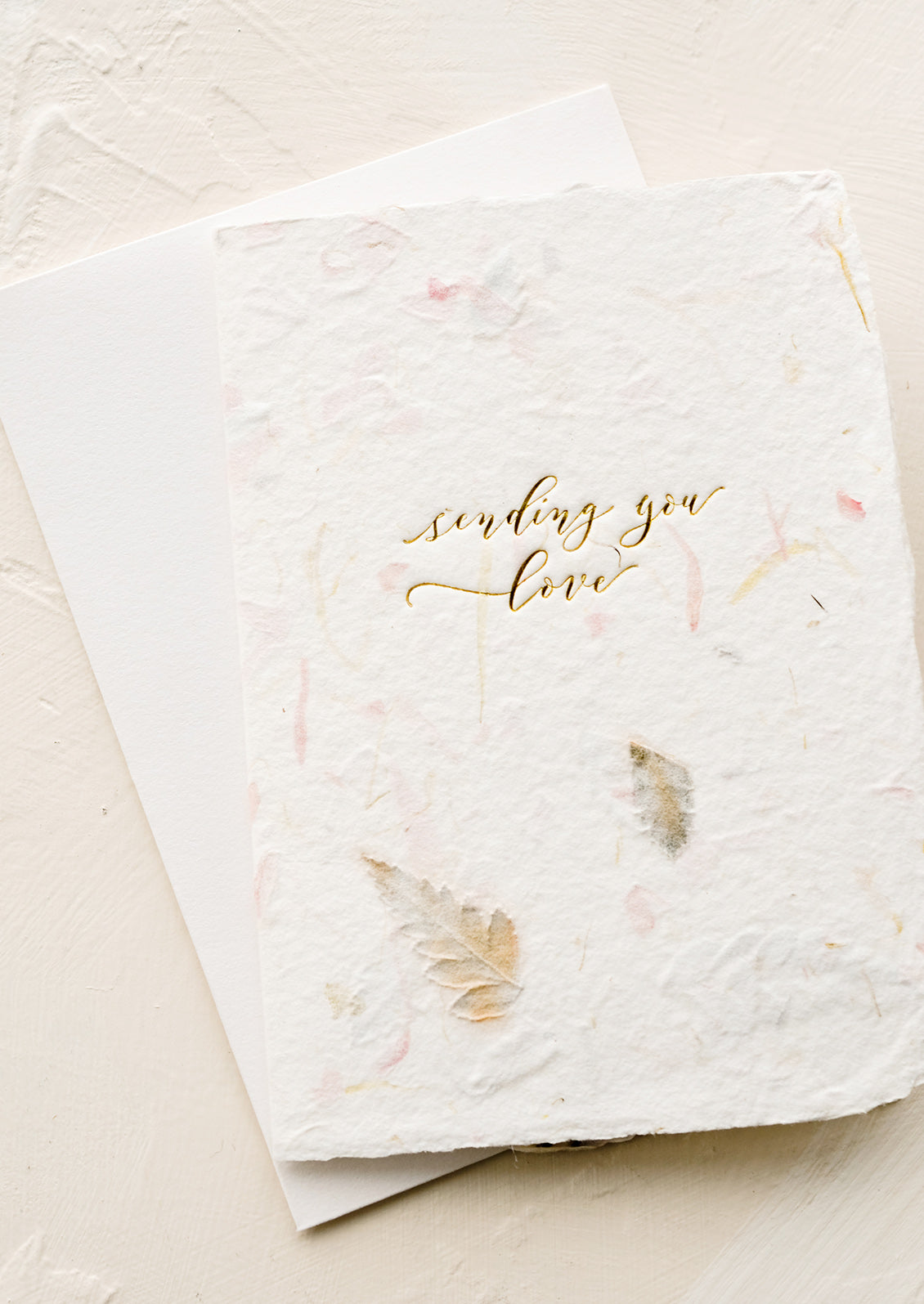 A greeting card made from handmade flower paper with gold script on front that reads "Sending You Love".