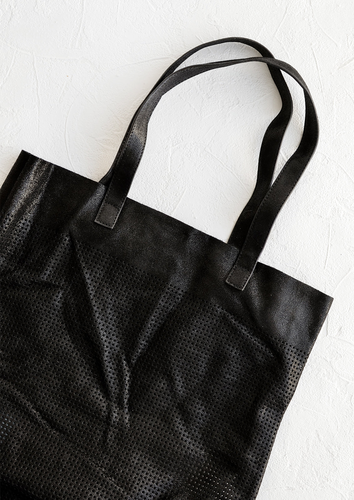A tote bag made from black colored shimmer leather with square perforation detailing throughout.