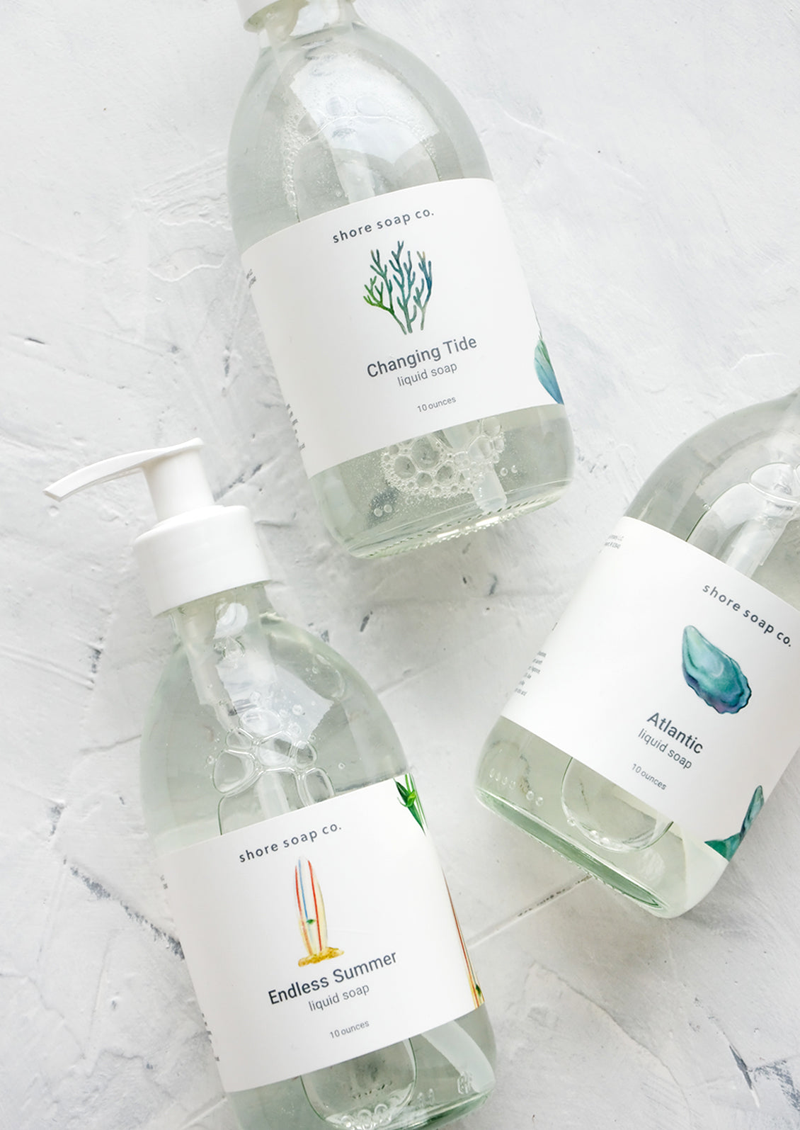 Glass pump bottles of liquid soap with nautical and beach themed labels and scents.