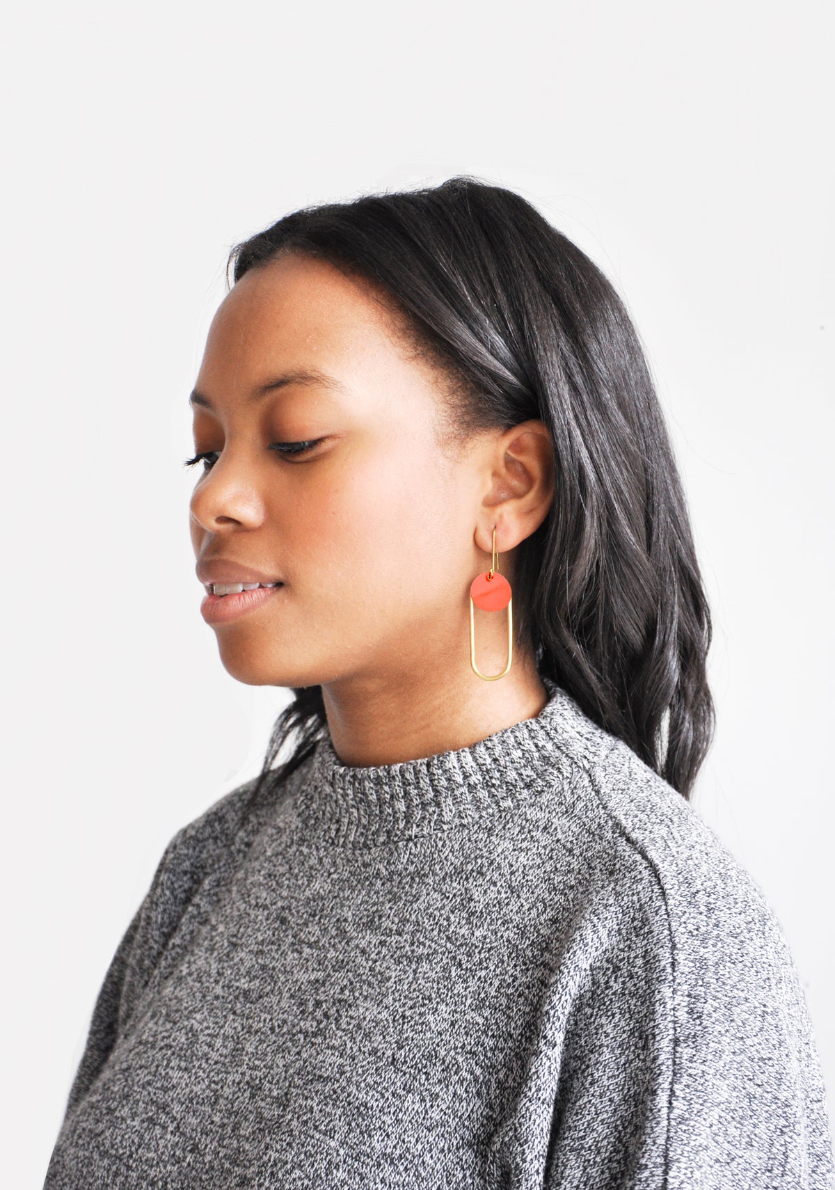 Woman modeling geometric, oval-shaped brass and enamel earrings.