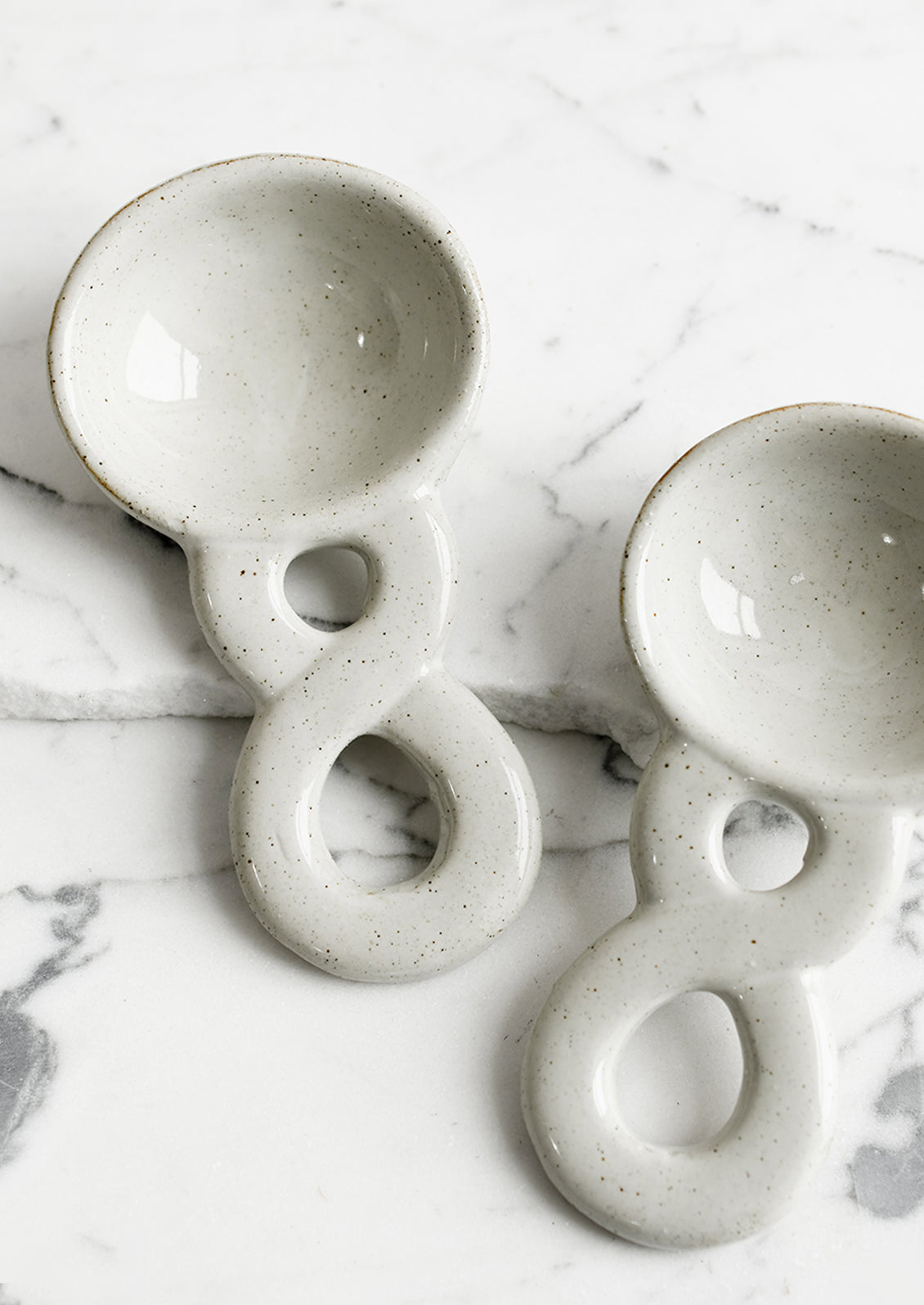 Two ceramic grey spoons with braided handle detail.