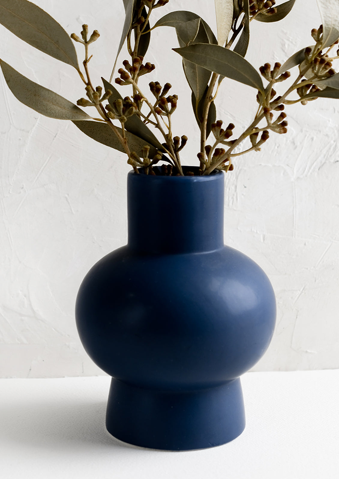 A navy blue sculptural ceramic vase with dried eucalyptus.