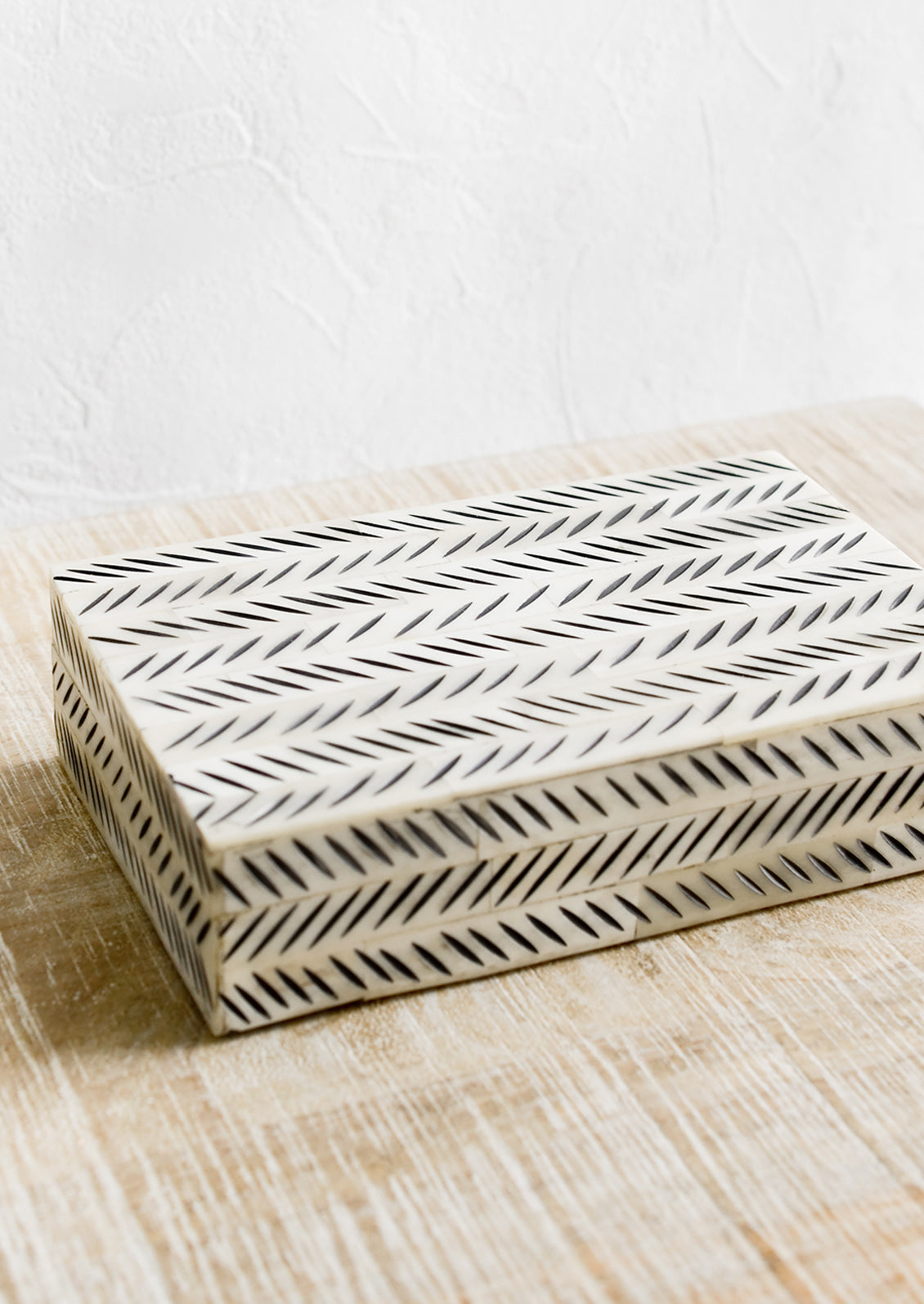 A decorative storage box made from ivory bone with black etched "slash" pattern.