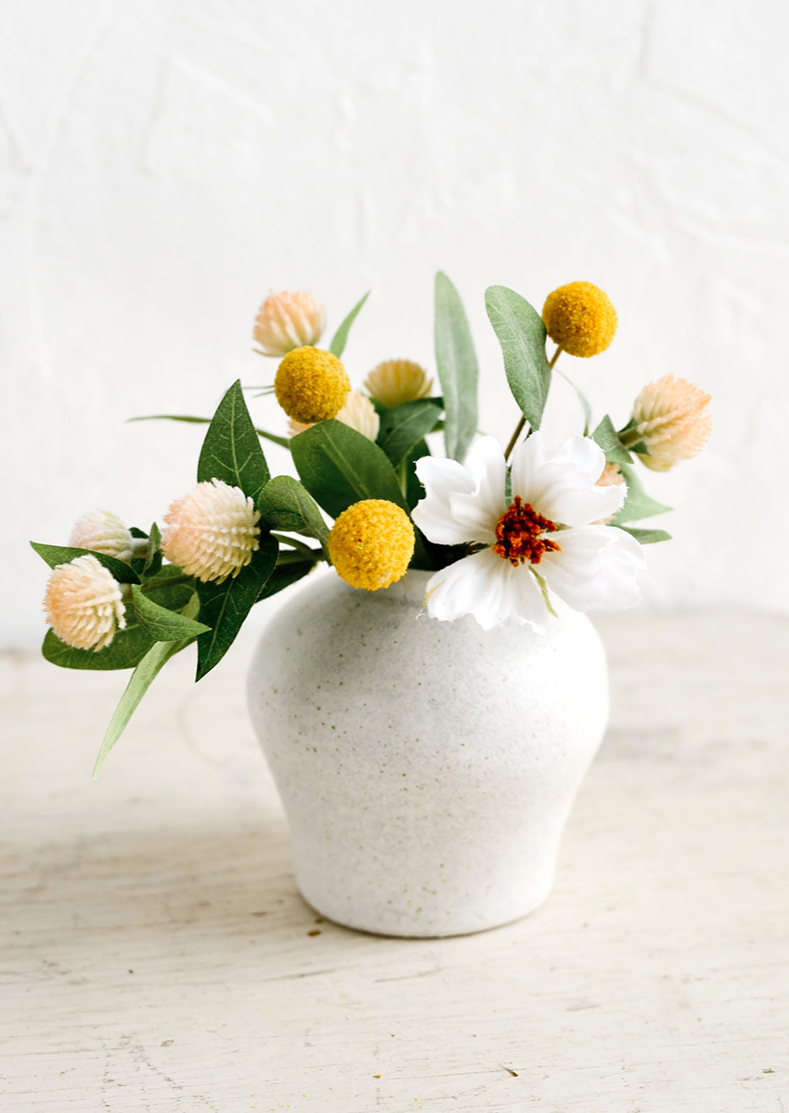 A small white ceramic vase in curvy shape with colorful flowers.
