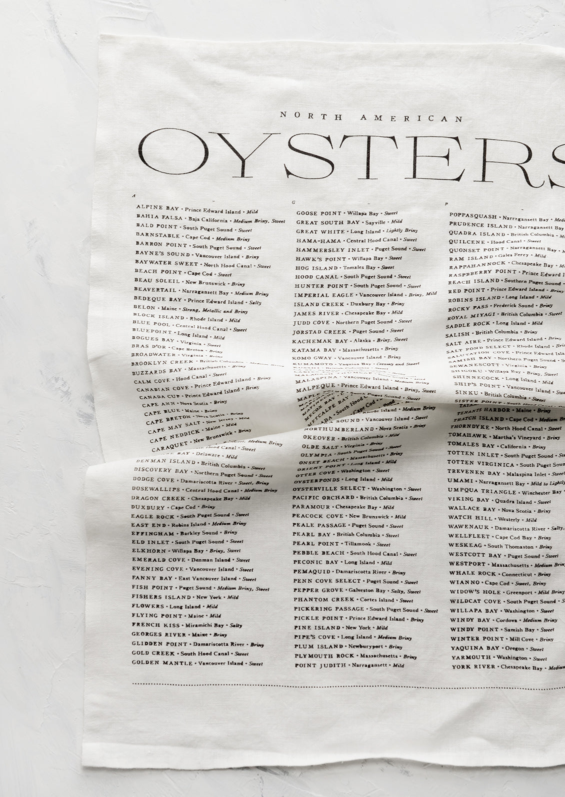 A white linen tea towel with black text listing out oyster types and their origins.