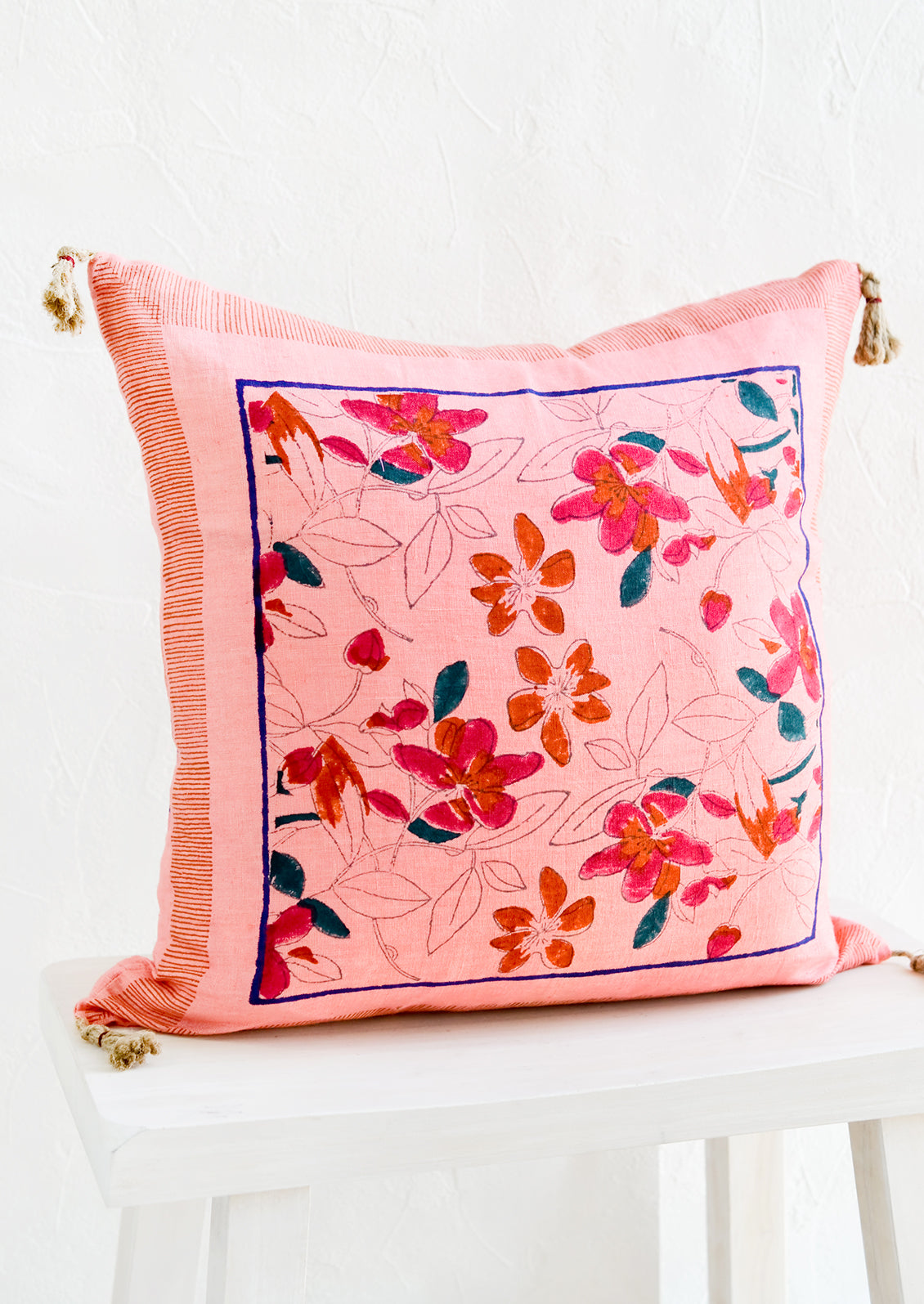 A square throw pillow in pink linen with a bordered floral block print pattern.