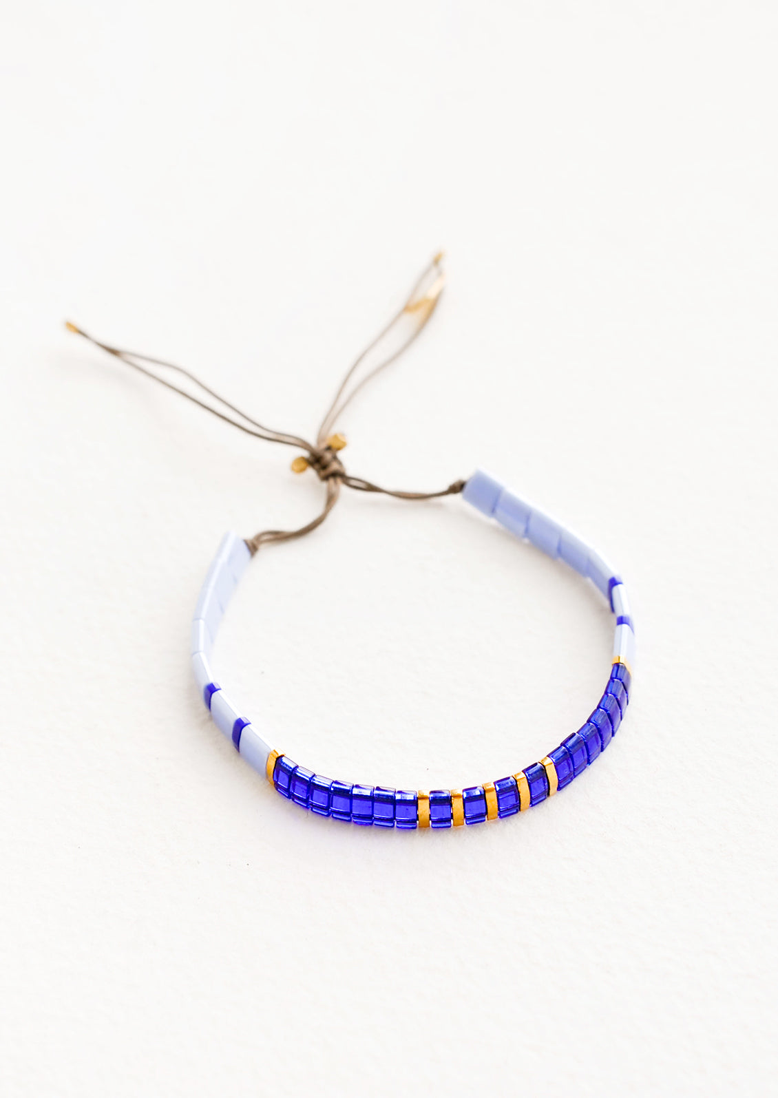 Bracelet featuring flat multicolor blue glass beads interspersed with flat gold bead on an adjustable cord.