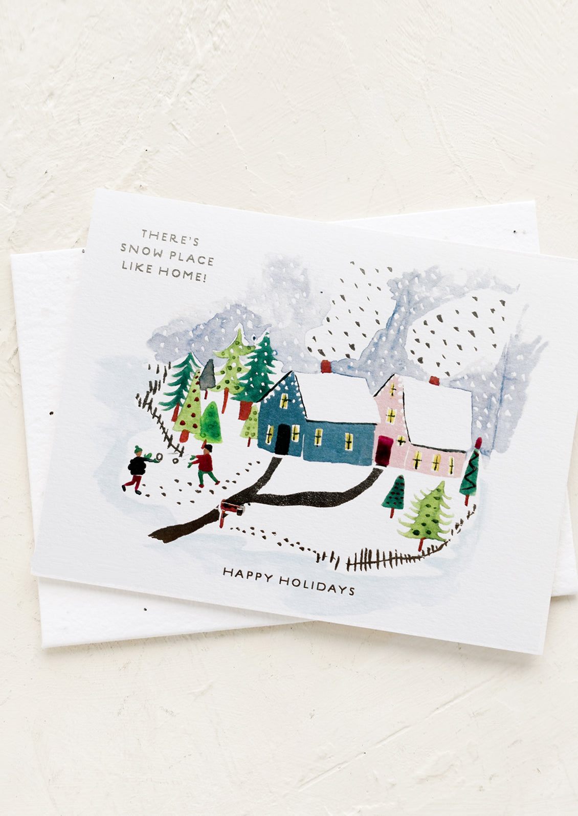 A greeting card with snowy village illustration, text reads "There's Snow Place Like Home!".