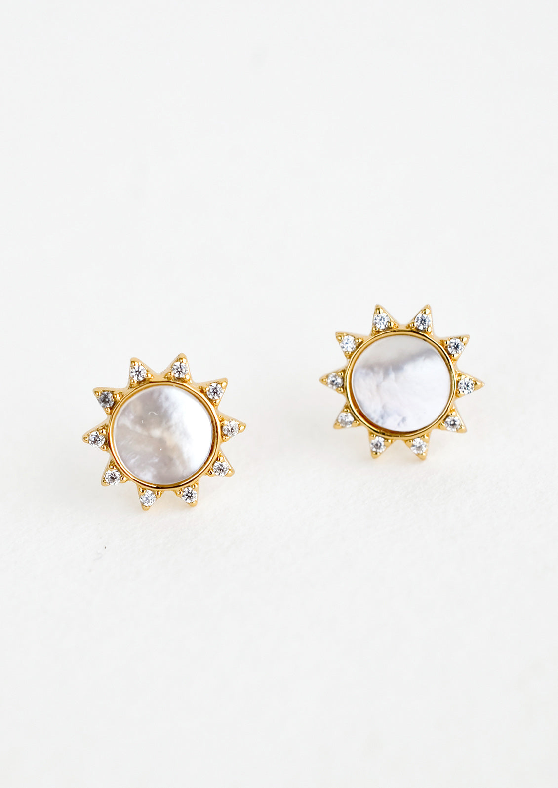 A pair of gold stud earrings in the shape of a sun with shell inlay center and crystal "sunray" border.