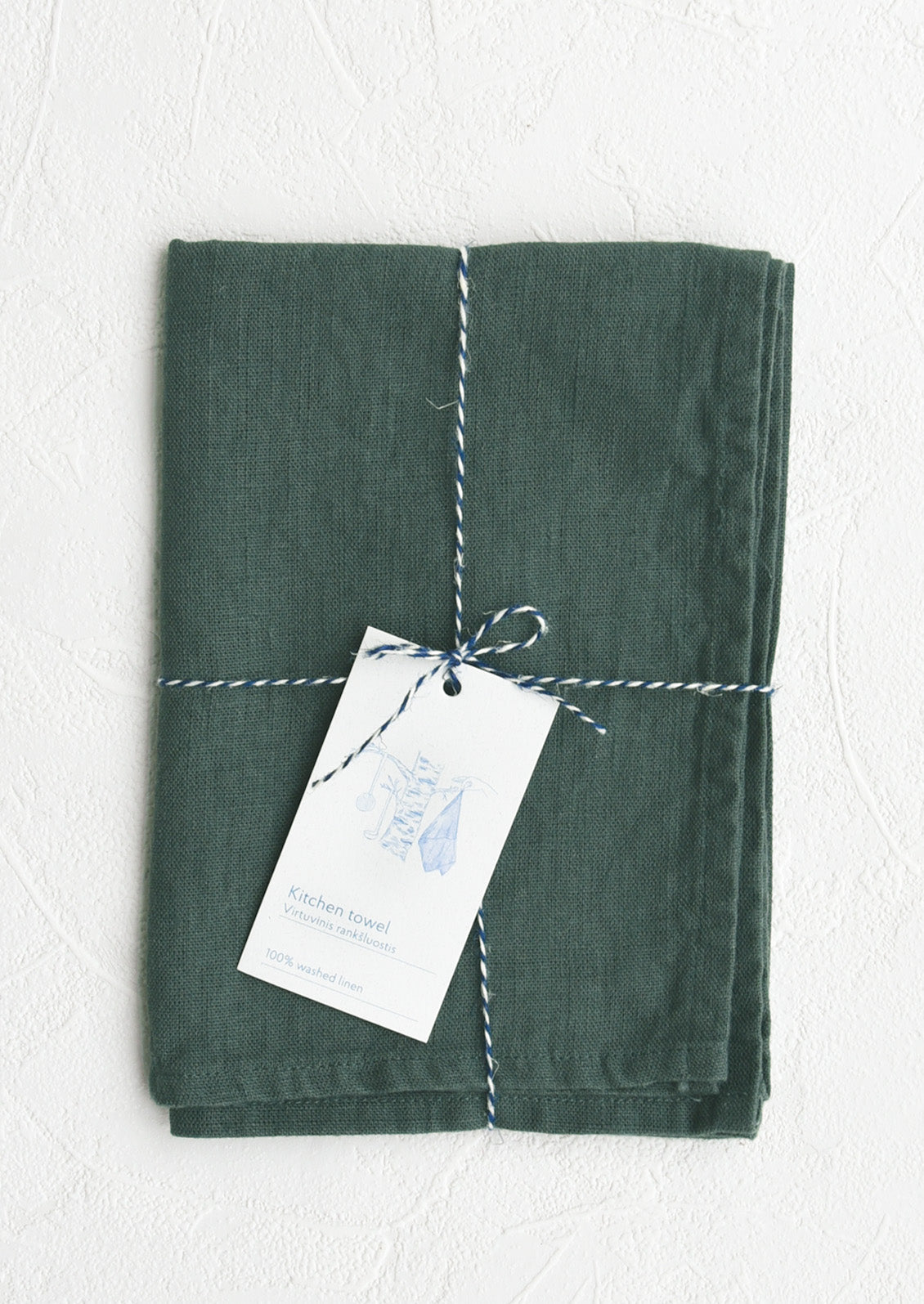 A folded dark teal linen tea towel tied in baker's twine with a decorative hangtag