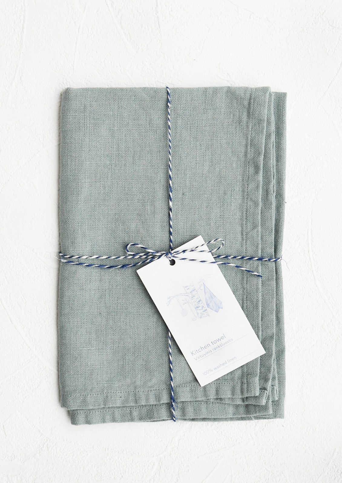 A folded faded pale blue linen tea towel tied in baker's twine with a decorative hangtag
