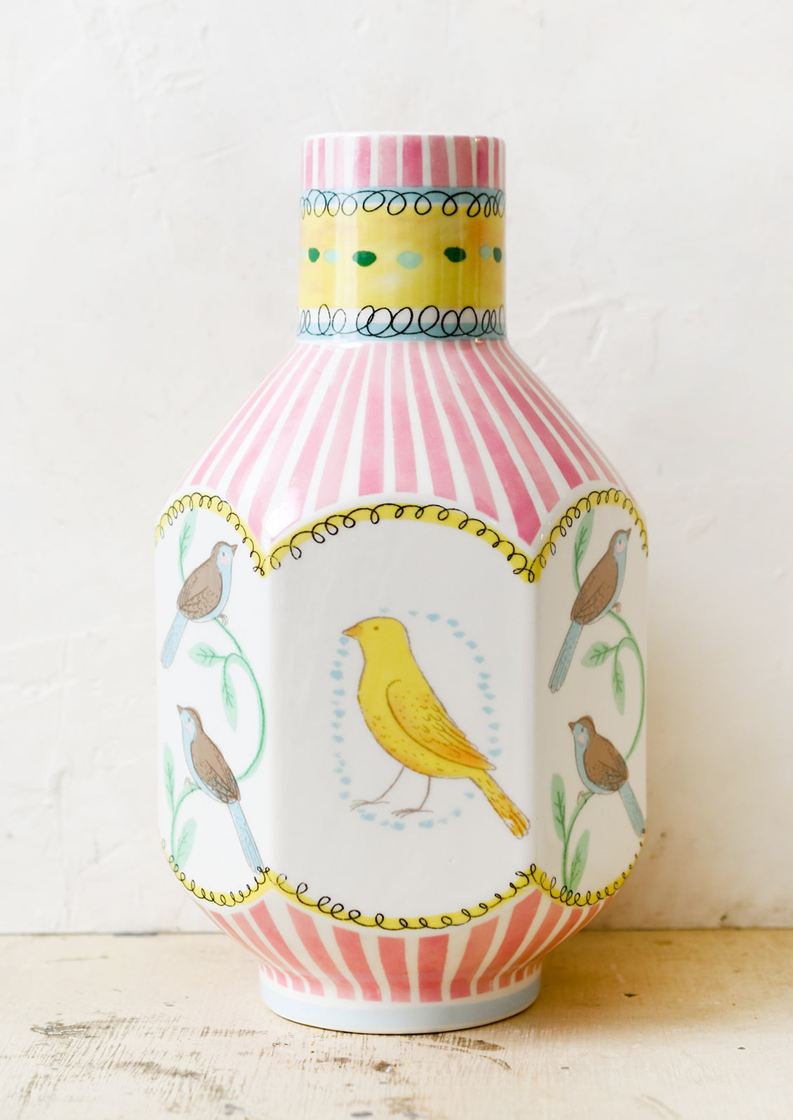 A graphic print vase with pink stripes and three-dimensional shape with bird motif.