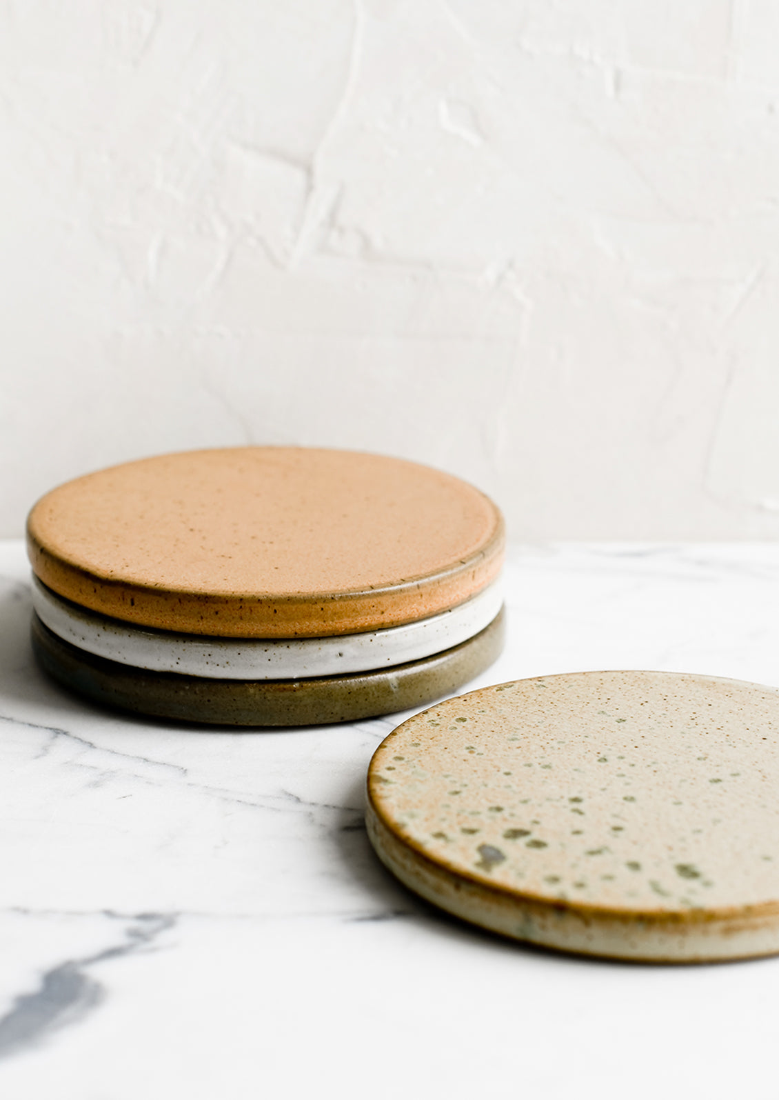 A set of four round ceramic coasters in earthy color mix.