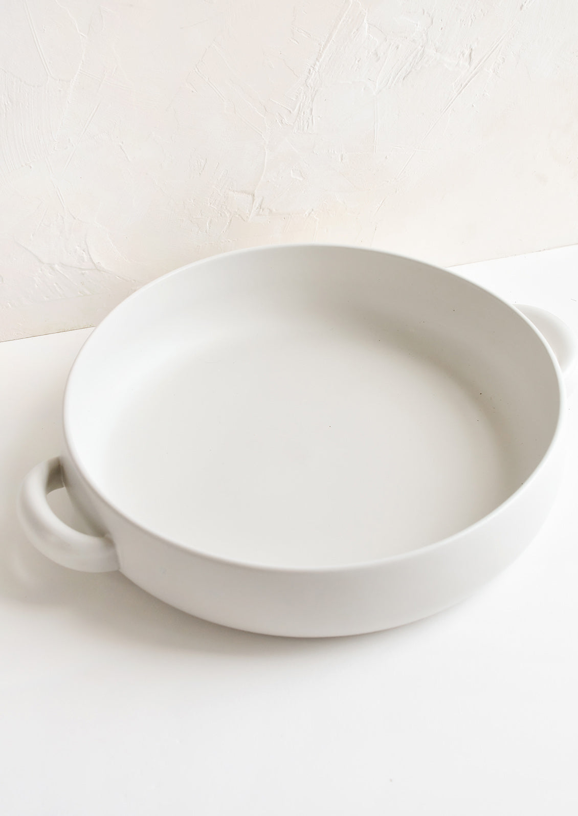 A round, shallow extra large serving bowl in white ceramic with curved handles at sides.