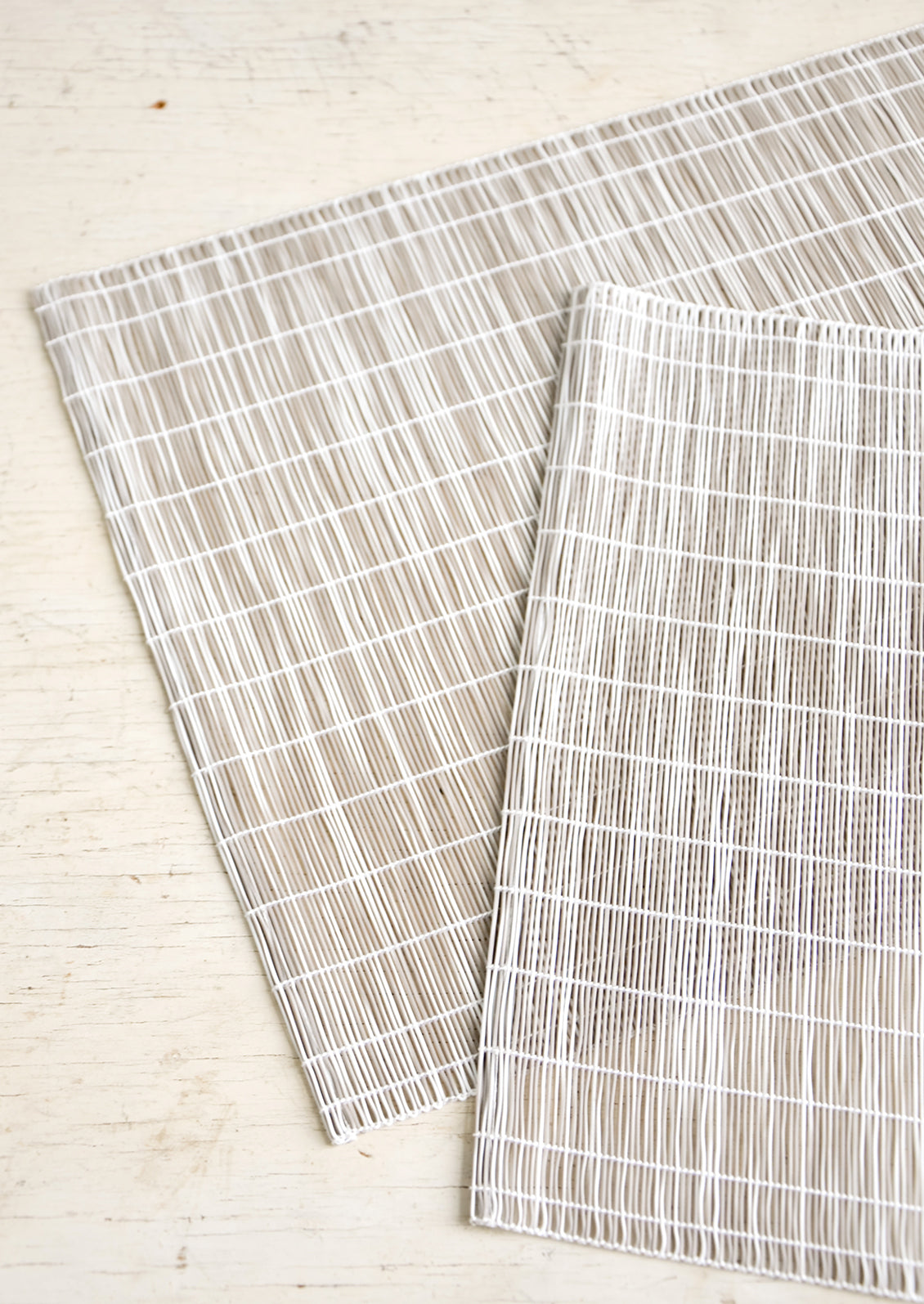 A pair of placemats made from intertwined, vertically woven vinyl in taupe and white.