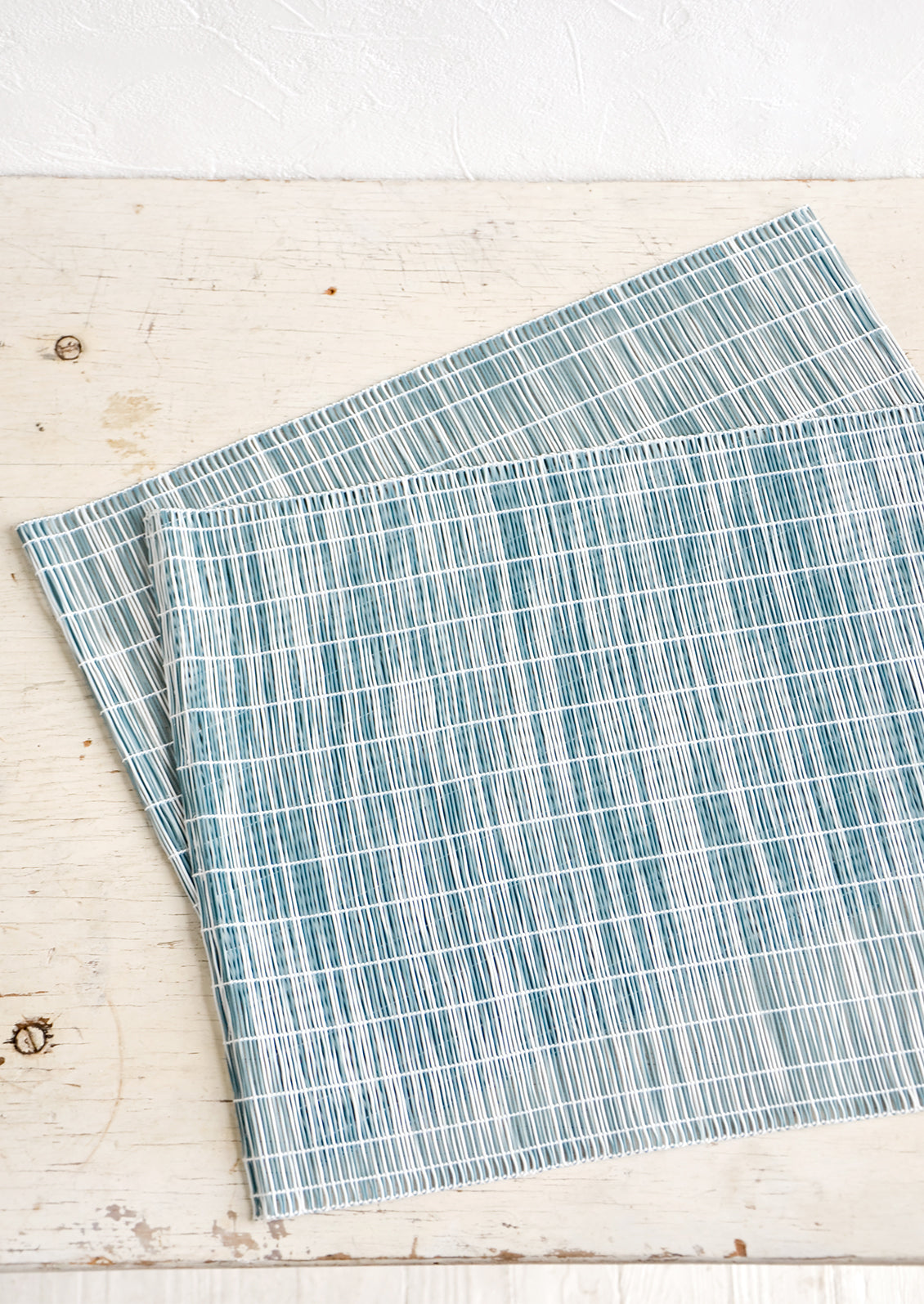 A pair of placemats made from intertwined, vertically woven vinyl in teal and white.