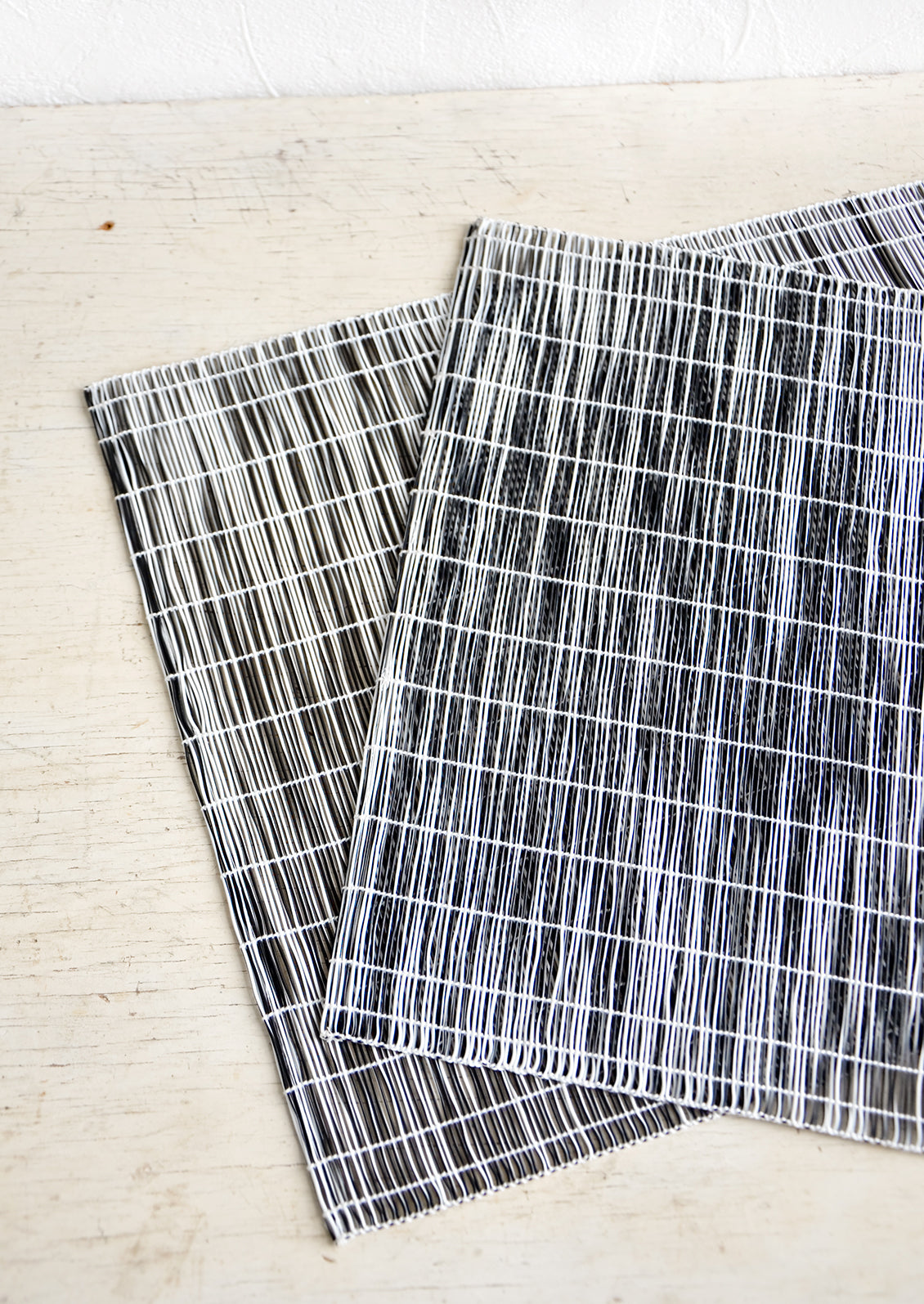 A pair of placemats made from intertwined, vertically woven vinyl in black and white.