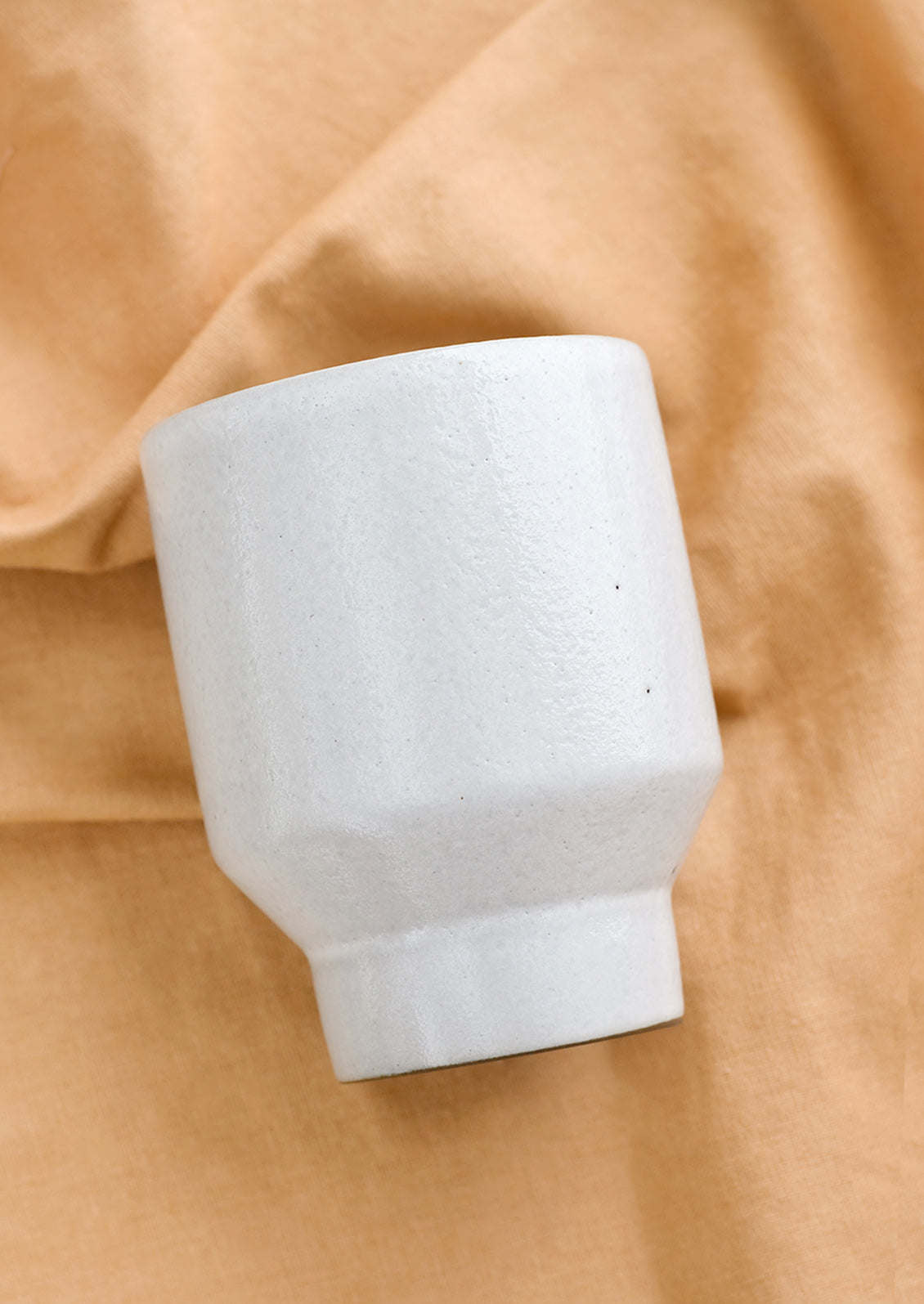 A white ceramic cup with a tapered base on brown fabric.