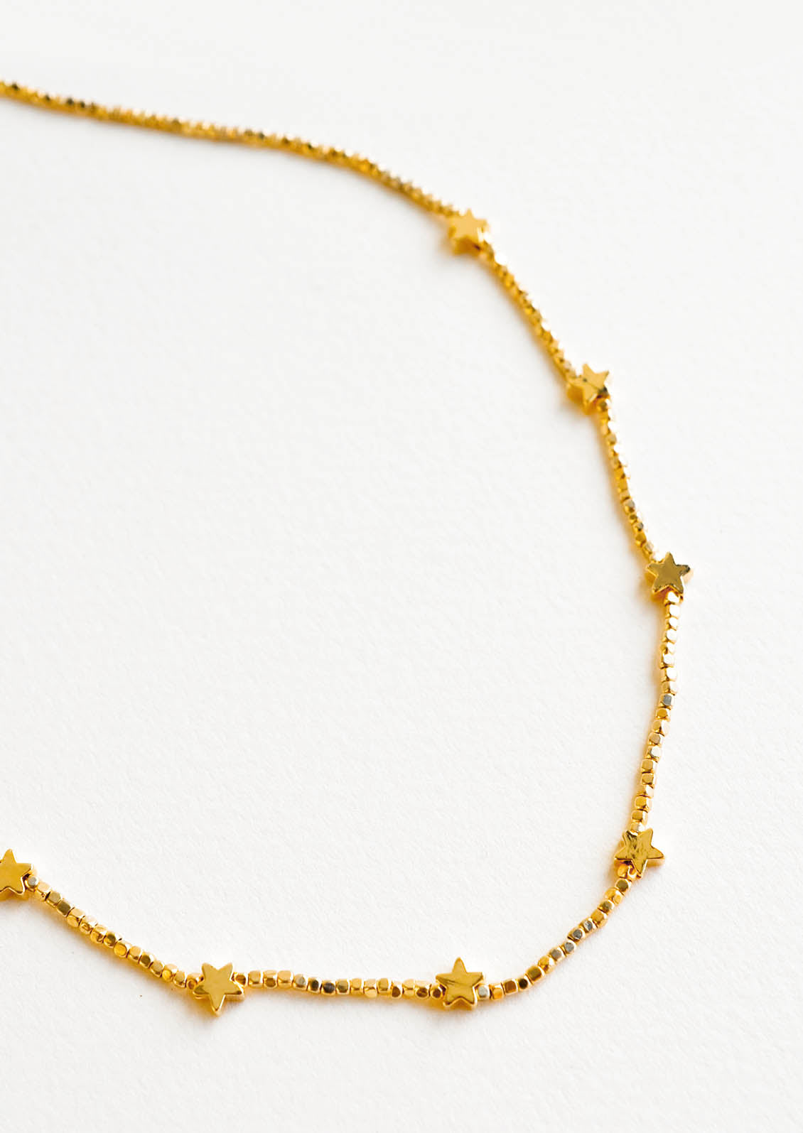 Close up shot of short necklace featuring round yellow gold beads interspersed with gold star beads and an adjustable closure.
