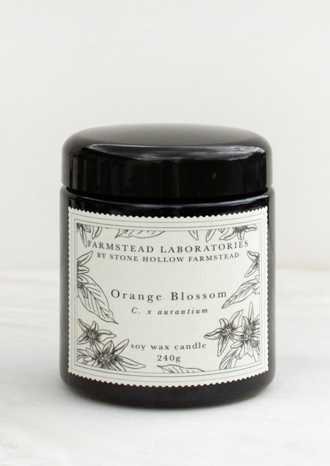 An orange blossom scented candle in black jar with black and white botanical label.