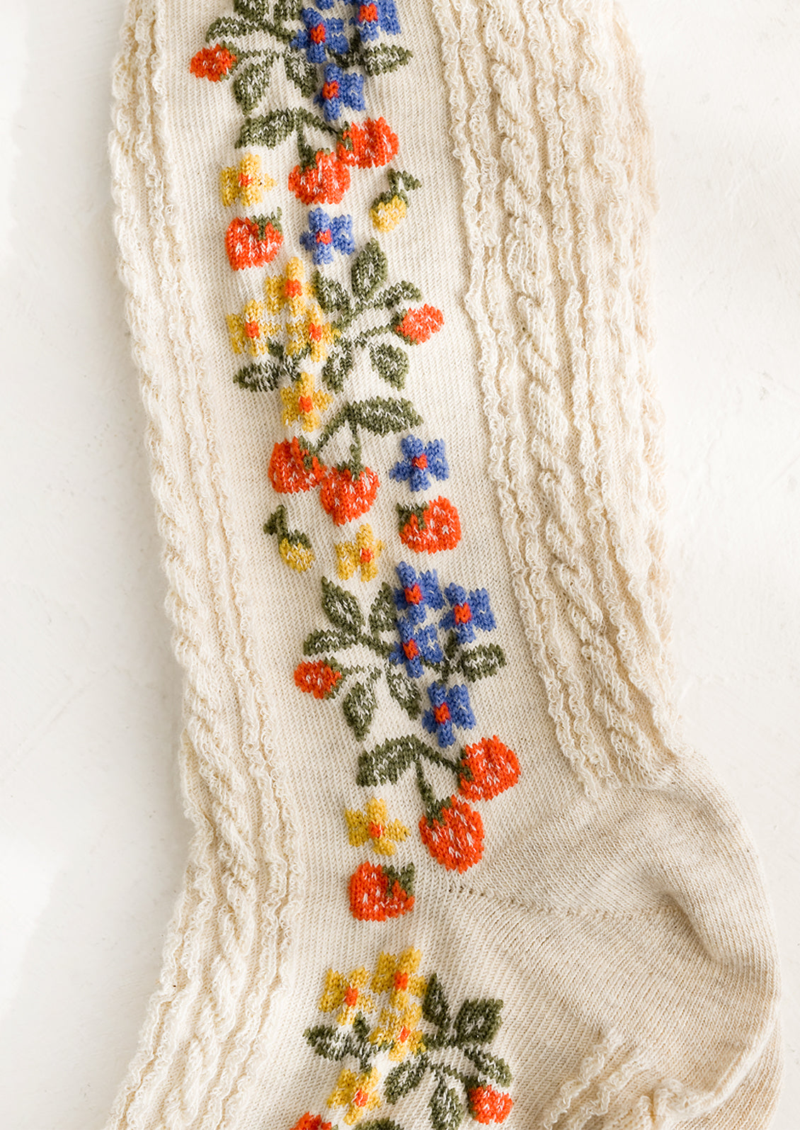 A pair of oatmeal colored socks with primary color strawberry print.