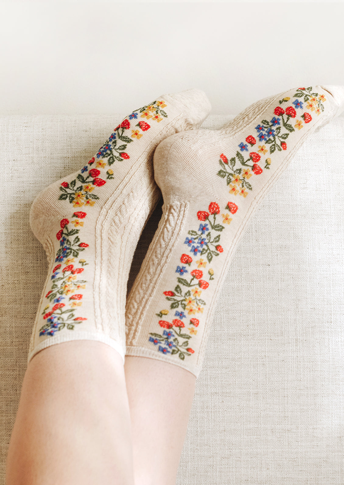 A pair of oatmeal colored socks with primary color strawberry print.