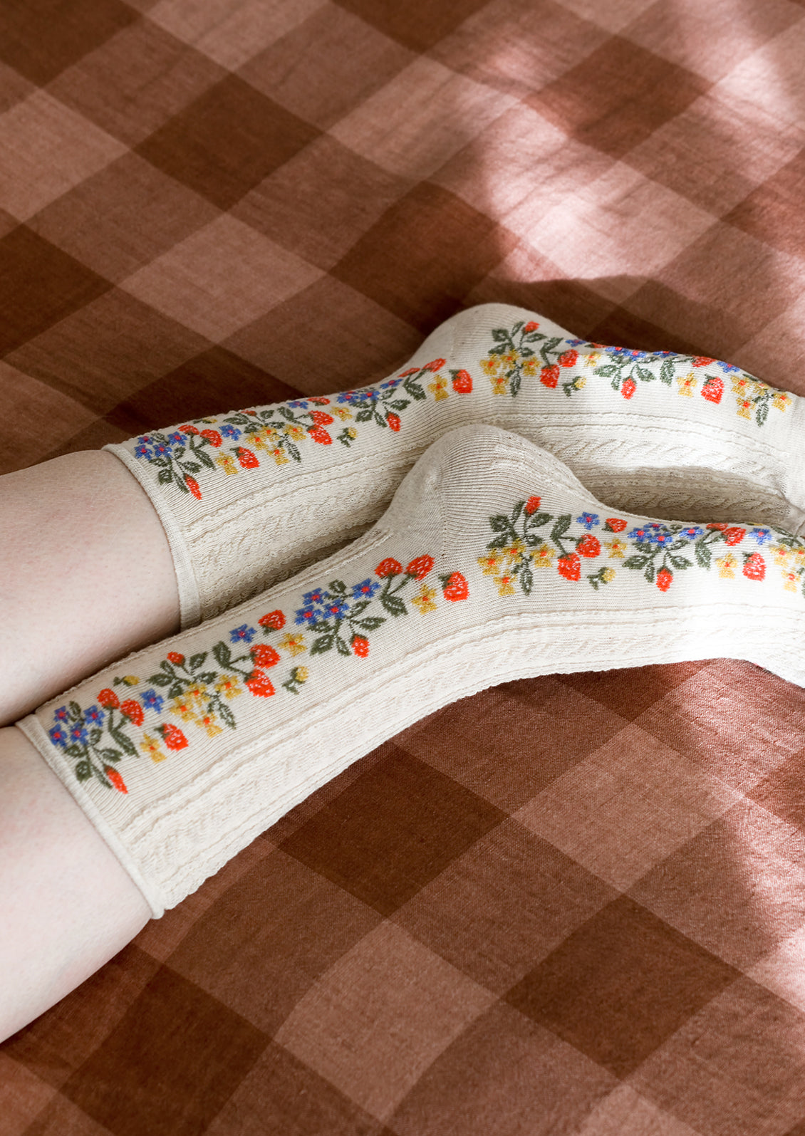 A pair of oatmeal colored socks with primary color strawberry print.