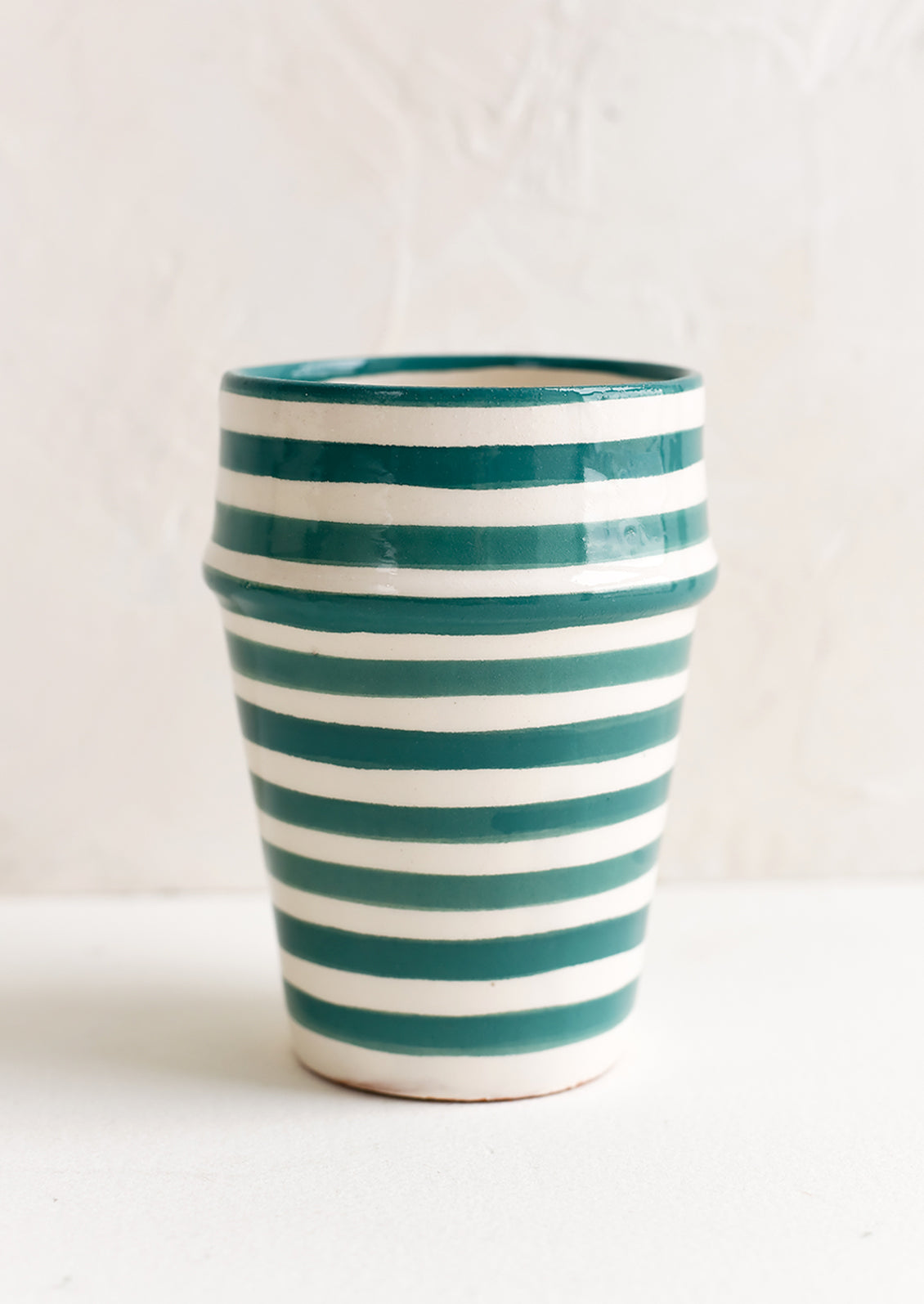 A moroccan style ceramic cup in teal and white stripes.