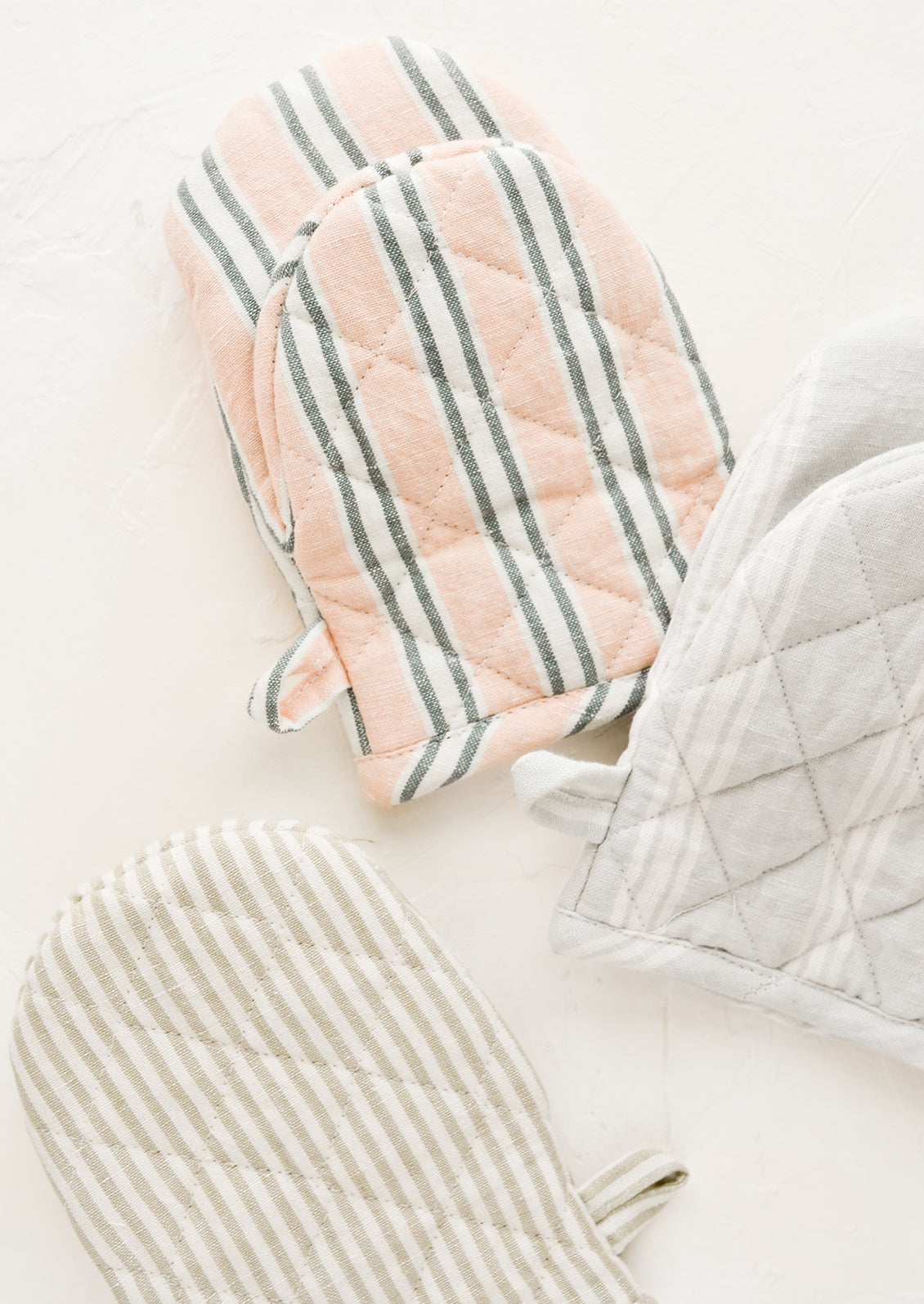 Three quilted oven mitts made from different colors of striped linen.