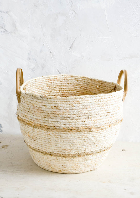Round storage basket woven from natural maize fiber with tan stripes and leather handles at sides
