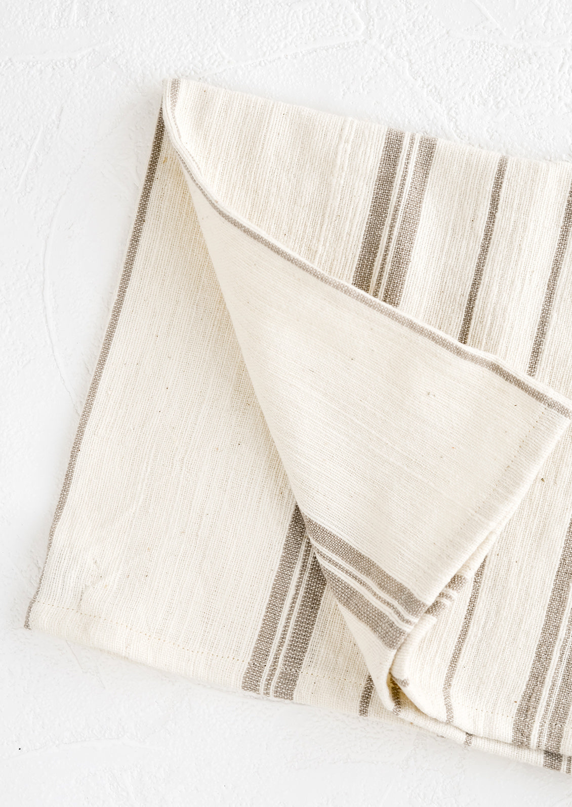 A folded natural cotton hand towel with taupe stripes.