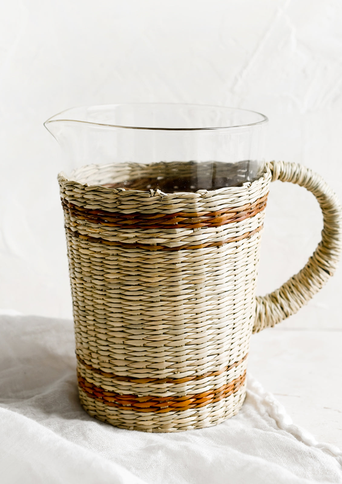 A glass pitcher with striped seagrass cloak and handle.