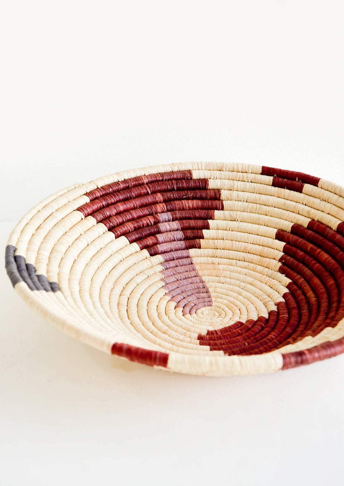 Shallow woven raffia bowl with abstract pattern in lavender, wine and charcoal